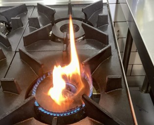 Photo of a commercial cooking appliance over gassed (not commissioned), excessive gas flow creates carbonisation of the flame. Gas fitter instructed to return and commission cooker