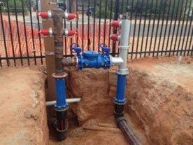 Photo of a Fire Service Installation with Backflow Prevention Device, with large installation pipes coming out of a hole in the ground